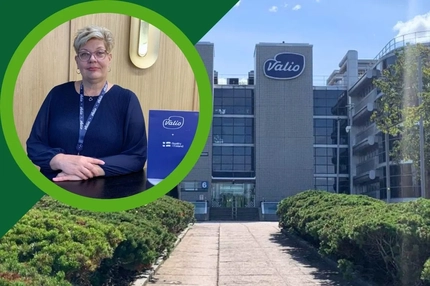 Image Valio video thumbnail: Woman wearing a Valio lanyard seated beside Valio branding, with a Valio office building and landscaped entrance in the background