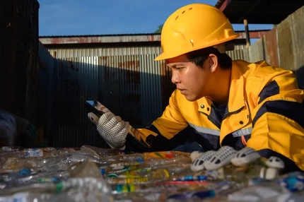 Image A person wearing a hard hat and gloves working on plastic recycling is looking at a cell phone