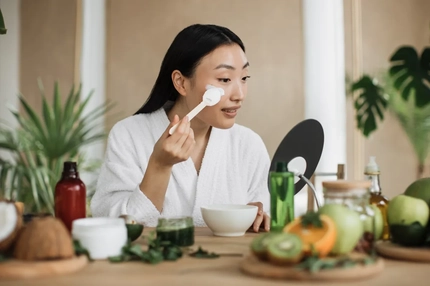 Image A woman swiping a cream on her face while looking in the mirror.