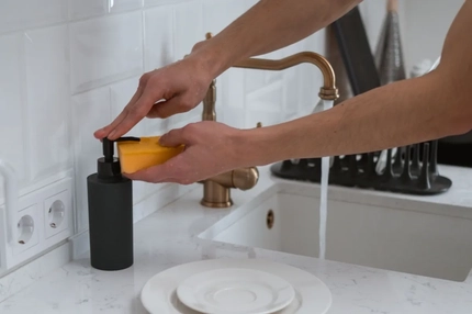 Image hands dispensing soap from a black pump bottle onto a yellow sponge