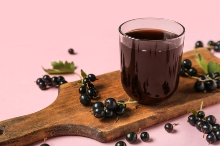 Image Glass of blackcurrant juice on a chopping board with blackcurrants.