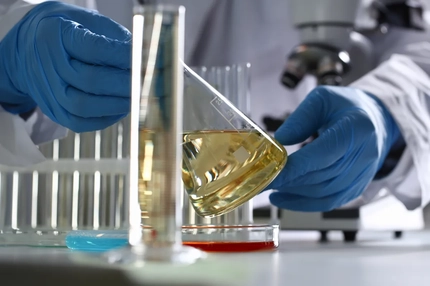 Image close up of researcher in lab coat wearing gloves holding a beaker oil oil