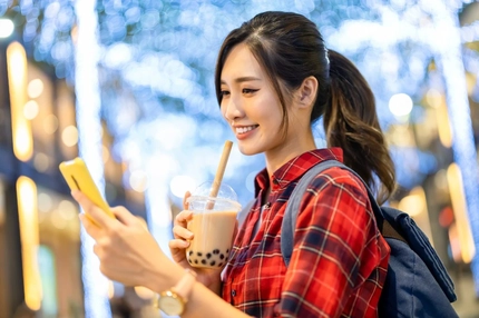 Woman drinks boba bubble tea while looking at her phone.