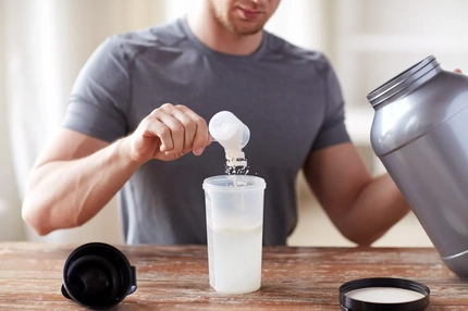 Image A man adds protein to a shaker cup from a large bucket of powder.