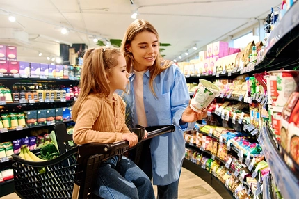Image Mother showing food product to daughter while shopping together in supermarket.