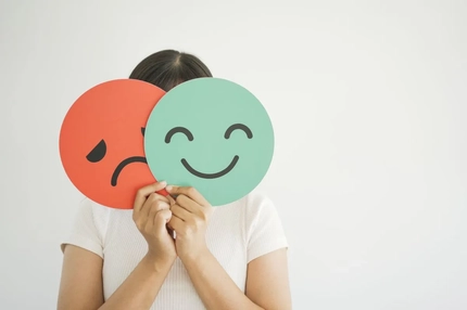 Image woman holding happy and sad emoji over face