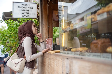 Muslim woman choosing pastries at coffee shop in Bali.