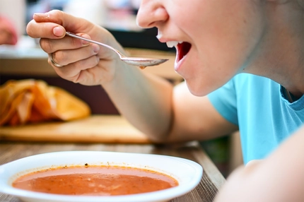 Image Woman eating tomato soup with spoon at home in kitchen.
