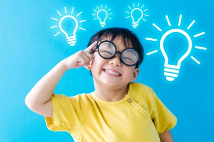 boy wearing glasses, smiling points his index finger to his head, with light bulbs above his head