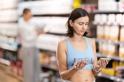 Image A woman compares ingredients on two protein bars in a store.