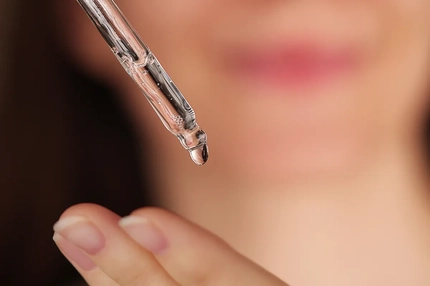 A dropper of oil going onto a woman's fingertips.