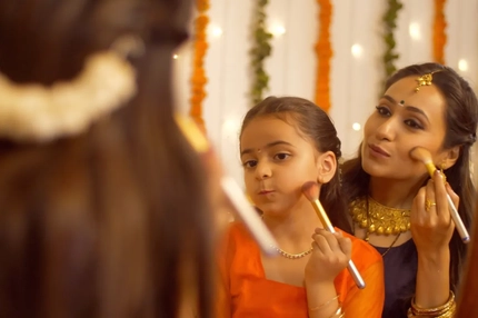 A mother and daughter doing their makeup in the mirror.