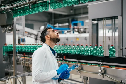 Image Male worker in bottling factory checking water bottles before shipment. Inspection quality control.