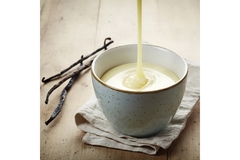Image Vanilla sauce being poured into a ceramic bowl with vanilla beans on a rustic wooden table.