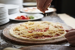 Image Person sprinkling cheese on a freshly prepared pizza dough