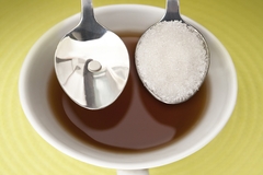 Image Two spoons over a cup of tea, one with white sugar and the other with a sugar substitute tablet.