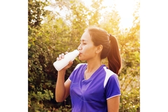 Image Woman hydrating with a bottled drink in sunlight