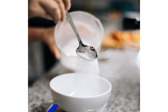 Image Hand pouring white sugar from spoon into bowl on kitchen counter