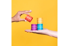 Two hands holding various vibrant lip balm containers.