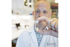 Image A scientist in a lab coat holds up a small bottle, possibly containing a chemical solution.