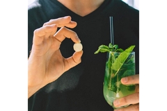 Image A man holding a mojito glass in one hand and a pill in the other hand.