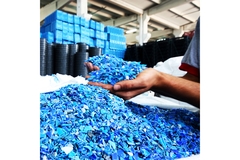 Hands holding bright blue recycled polypropylene flakes in an industrial recycling facility