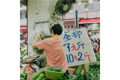 Image A man standing in front of a variety of farm-fresh produce at a market stall