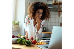 Image Woman preparing food and looking at her laptop screen.