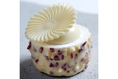 a round, artisan white chocolate with dried red fruit on the sides and a fanciful white chocolate hat that looks like lace.