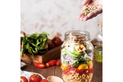 Image Hand adding seeds to a jar of vegetables.