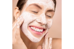 Image A woman smiles while applying a beauty mask to her face.