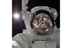 An astronaut floats in space with the sun behind him.