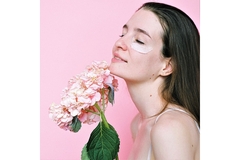 Image A woman with face cream on her cheeks closes her eyes and smiles while holding up a bouquet of flowers.
