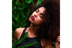 A woman smiles while closing her eyes while large green leaves surround her.