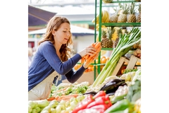 Image enthusiastic woman grabbing 3 carrots from a display outside.