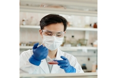 Scientist in a lab with a pipet and petri dish.