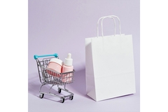 Image A miniature shopping cart is filled with cosmetics products and positioned next to a white shopping bag.