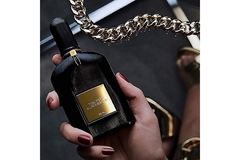 A woman with painted nails holds bottle of Tom Ford perfume.