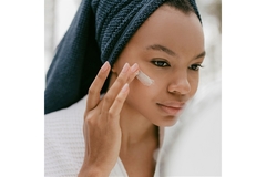 A woman with her hair wrapped in a towel applies a face cream.