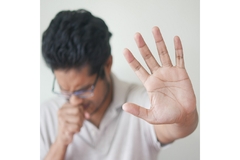 Image A person coughs and holds up their hand to ward others off.