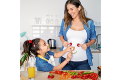Image Woman and child in kitchen making a smiley face out of vegetables on the woman's stomach.