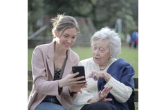 Image Old and young woman sitting on park bench and looking at phone.