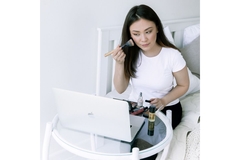 woman applying makeup while looking into laptop