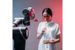 Image A woman smells a flower while a large robot arm is positioned in front of her.