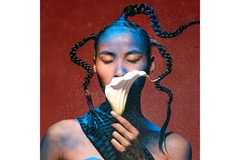 Image A woman with her hair in braids and colorful makeup smells a flower.