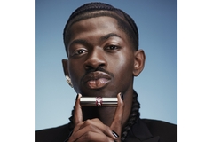 Rapper Lil Nas X poses with a full face of makeup while holding up a YSL lipstick.
