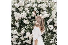 woman wearing a hat in front of a white rose bush