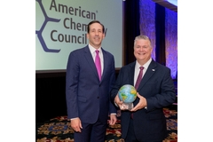 Image Two men standing and smiling while one is holding a small globe.