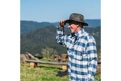 Image Farmer holding his hat, standing in a field with mountains in the background.