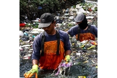Image two men waist deep in a water body with marine plastic waste surrounding them
